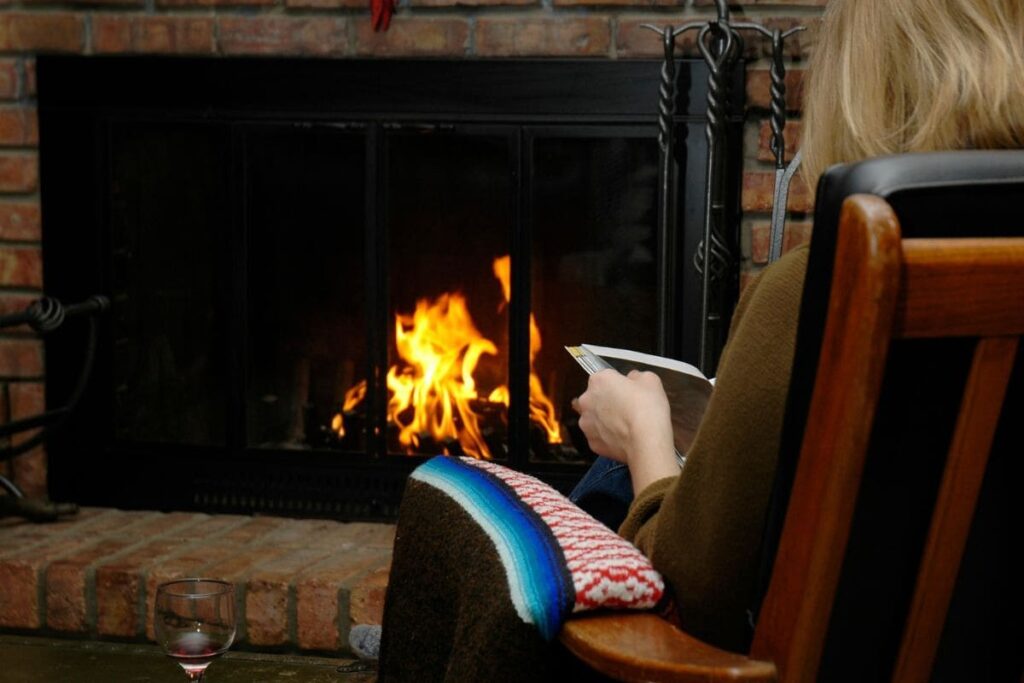 Lady relaxing by an open fire in an armchair reading a book